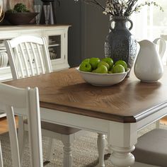 a bowl of green apples sitting on top of a table next to a white chair