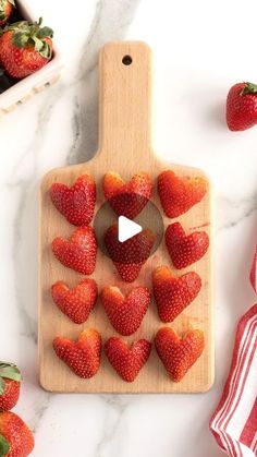 strawberries arranged in the shape of hearts on a cutting board