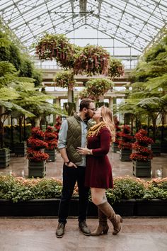 an engaged couple standing together in the middle of a greenhouse