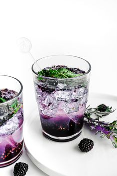 two glasses filled with ice and blackberries on top of a white plate next to each other