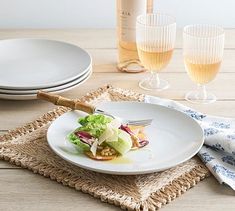 a white plate topped with lettuce next to two wine glasses and a bottle