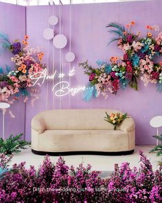 a couch sitting in front of a purple wall with flowers hanging from it's sides