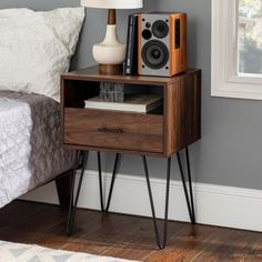 a nightstand with speakers on it next to a bed in a room that has gray walls