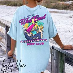 California surf T-shirt. Skeleton surfing on the back with a small pocket design in front. Perfect tee to wear this summer or all year round. Perfectly preppy attire. To wear this oversized, size up 1-2 sizes. *Unisex sizing. Please see size chart in photos*  No side seams mean there are no itchy interruptions under the arms. The shoulders have tape for improved durability. .: 100% cotton (fiber content may vary for different colors) .: Medium fabric (5.3 oz/yd² (180 g/m .: Classic fit .: Tear-away label .: Runs true to size Blue Beach T-shirt With Front Print, Blue Summer T-shirt For Surfing, Summer Streetwear Tops With Back Print, Trendy Cotton T-shirt For Surfing, Relaxed Fit T-shirt With Back Print For Summer, Beachy Crew Neck T-shirt For Surfing, Summer Surfing Vsco T-shirt, Trendy Short Sleeve T-shirt With Back Print, Casual Blue T-shirt With Back Print