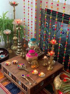 a wooden table topped with lots of colorful beads and jewelry next to a fireplace covered in potted plants