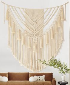 a living room with a brown couch and macrame wall hanging on the wall