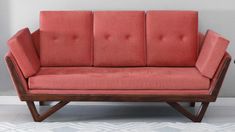 a red couch sitting on top of a white rug next to a wooden frame chair