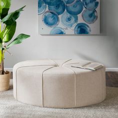 a round ottoman sitting on top of a white rug next to a potted plant