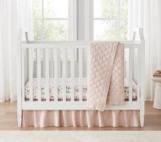 a white crib with pink bedding and curtains