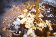 the food is being cooked in the pot on the stove top with a yellow liquid pouring into it