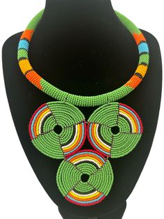 This stunning African necklace showcases a beautiful green beaded disc pendant that is truly authentic. The pendant is handcrafted and features intricate beading detail that is sure to impress. The necklace is perfect for those who appreciate the fine craftsmanship and unique jewellery. The beaded pendant is eye-catching and adds a touch of elegance to any outfit.  The diameter of the pendant - 5 inches. Neck Width - 16 inches. Adjustable Green Artisan Jewelry, Green Adjustable Artisan Jewelry, Artisan Adjustable Green Jewelry, Traditional Green Adjustable Necklace, Unique Green Necklace With 108 Beads, Multicolor Beaded Necklaces With Large Round Pendants, Handmade Green Bohemian Beaded Necklaces, Adjustable Green Beaded Necklace, Bohemian Green Pendant Beaded Necklace