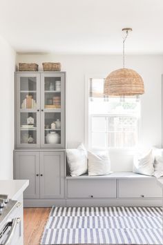 a white and gray kitchen with lots of cabinets in the corner, including a window seat