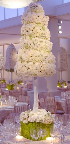 a tall white flower arrangement on top of a table in a room with tables and chairs