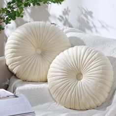 two white pillows sitting on top of a bed next to a book and potted plant