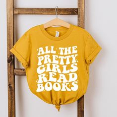 Looking for a cute tee for your kids? We have the perfect Pretty Girls Read Books graphic tee addition to their closet! Also available in toddler tees. Bookish Graphic Print Tops For School, School Tops With Graphic Print In Bookish Style, Bookish Text Print Tops For School, Books Graphic, Girls Graphic Tee, Girl Reading, Toddler Tees, Fitness Fashion, Sleeve Styles