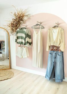 clothes are hanging on the wall in front of a mirror, and two women's clothing hang from hooks