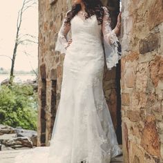 a woman in a wedding dress leaning against a stone wall