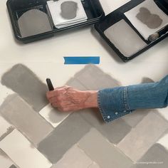 a person with their hand on a paintbrush next to two trays of paints