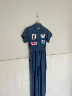 a very rare 1970s denim jumpsuit. features all the original patches from 1970s owner, collared neckline and hidden button up closure up the front. this is a one of a kind jumpsuit with the most amazing collection of patches.  measurements are taken with garment lying flat. Please note there is no stretch to denim.  bust 34' shoulder 5' sleeve 6' length from waist to shoulder 28' waist 25' inseam 30.5' Retro Cotton Denim Jumpsuit In Medium Wash, Retro Medium Wash Cotton Denim Jumpsuit, Retro Cotton Short Sleeve Jumpsuit, Retro Jumpsuits And Rompers With Pockets, Retro Cotton Fitted Jumpsuits And Rompers, Retro Short Sleeve Jumpsuits And Rompers With Pockets, Fitted Jumpsuits And Rompers With Patch Pockets For Spring, Retro Denim Overall Jumpsuit, Retro Denim Overalls Jumpsuits And Rompers