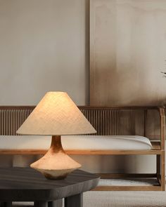 a lamp sitting on top of a wooden table next to a white bed in a room