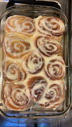 a glass dish filled with cinnamon rolls covered in icing