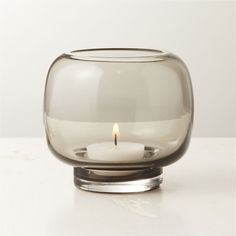 a glass candle holder with a single lit candle inside it on a white countertop