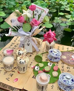 an arrangement of teacups and flowers on a table in front of water lilies