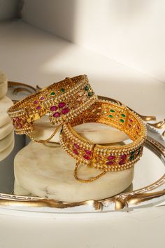 Introducing the Amika Bangle Set (Set of 2), a stunning addition to any jewelry collection. These gold-plated bangles feature intricate designs adorned with pearls and vibrant multicolor stones, including green and ruby accents. The detailed floral and petal patterns exude elegance and sophistication, making these bangles & bracelets set perfect for desi weddings and special occasions. The Amika Bangle Set showcases the timeless beauty of Navratan craftsmanship. The bangles are designed with an Navratan Bangles, Bangles And Bracelets, Bangles Set, Gold Plated Bangles, The Bangles, Bangle Bracelet Set, Bracelets Set, Bangles Bracelets, Desi Wedding