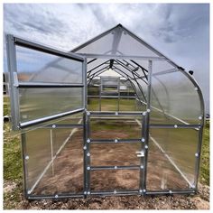 a large metal greenhouse in the middle of a field with grass and dirt on the ground