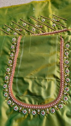 an embroidered green cloth with white flowers and beads on the border is laying on a gray surface