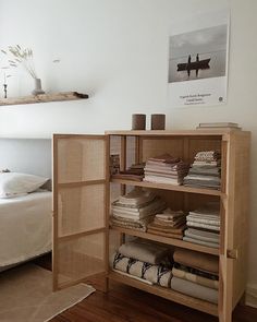 a book shelf filled with lots of books next to a white bed and wooden floor