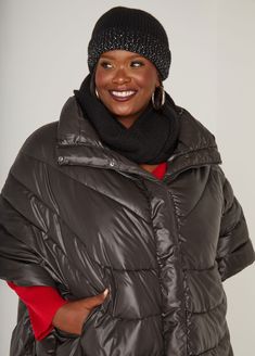 a woman in a black hat and coat smiles at the camera while standing with her hands on her hips