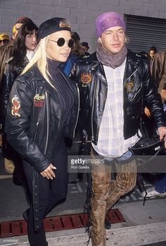 a man and woman in leather jackets are walking together on the street with other people behind them