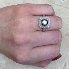 a woman's hand holding a ring with a diamond in the middle and an oval center surrounded by smaller diamonds