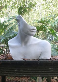 a white sculpture sitting on top of a wooden bench next to trees and leaves in the background