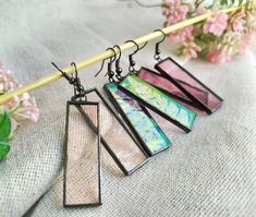 three different colored stained glass pieces hanging from a wooden stick with flowers in the background