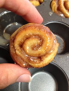 a hand holding a cinnamon roll in a muffin tin