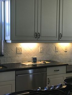 a kitchen with white cabinets and black counter tops is lit by recessed lights above the stove