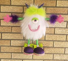 an odd looking stuffed animal hanging on a brick wall with purple and green shoes next to it