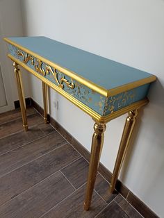 a blue and gold console table sitting on top of a wooden floor next to a white wall