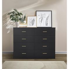 a black dresser with two pictures on top and a potted plant in the corner