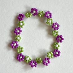 a purple and green beaded bracelet on a white surface with space for the letter o