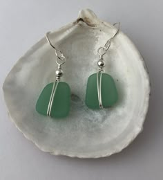 green sea glass earrings sitting on top of a seashell with silver earwires