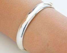 Most bangles are circular in shape , they are symbolic of planet Jupiter , Mercury , and the moon.  A truly classic piece, made of sterling silver. Modern, minimalist oval shape, it has a smooth inner making it a comfort fit bangle . The sides can be opened / closed on a pin hinge and puss-in latch for taking off and putting on.    The shape, weight and smooth finish of this bangle makes it lovely and tactile. Suitable for all occasions formal or otherwise and will complement any wardrobe. Silver Bangle With Sterling Silver Clasp, Silver Thick Band Bracelet With Polished Finish, Silver Bracelet With Thick Band And Polished Finish, Silver Bracelet With Polished Finish And Thick Band, Sterling Silver Jewelry With Shiny Finish, Bangle With Sterling Silver Clasp, Sterling Silver Jewelry With Shiny Round Band, Sterling Silver Rounded Jewelry With Polished Finish, Classic Round Bangle Stamped 925