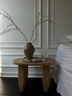 a vase with some flowers on top of a small table in a room that has white walls and wood flooring