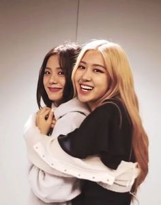 two young women hugging each other in front of a white background and one is smiling