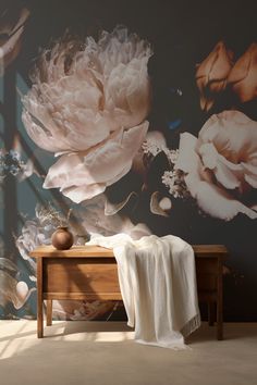 a wall with flowers painted on it next to a wooden table and white throw blanket