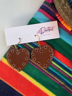 "Looking for lovely Latino-inspired polymer clay earrings? Grab this hand-painted pair of glazed cazuelita style, barro pottery heart earrings. Handmade here in the Alamo City, these Mexican-style earrings are perfect for a Valentine's date or any day you want to represent your love for your culture! These earrings are grand (1.5\") making them a beautiful statement piece. Each set is secured to 25k gold-toned, nickel-free clasp hooks. All earrings are lightweight and made of quality FIMO brand polymer clay, with the fine-detailed designs being hand-painted with acrylic. UV resin is used to lock in protection on the hand painted design. Properly fitted backings are included. Fall in love with this pair? Put it in your cart! Follow me @dovetailcraftique on Instagram, Facebook, TikTok, and P Mexican Style Clay Earrings, Artisan Heart Earrings For Pierced Ears As Gift, Hand Painted Dangle Heart Earrings As Gift, Artisan Heart Earrings As Gift, Heart Beads Polymer Clay Jewelry Gift, Heart-shaped Polymer Clay Earrings For Valentine's Day, Unique Hand Painted Heart Earrings, Valentine's Day Heart-shaped Polymer Clay Earrings, Unique Heart Earrings For Valentine's Day Gift