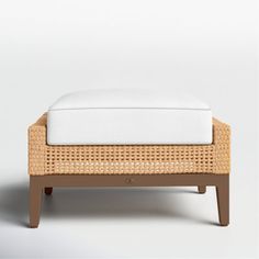 the foot stool is made out of wicker and has a white cushion on it