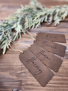 three leather tags with writing on them sitting next to a pine branch and evergreen needles